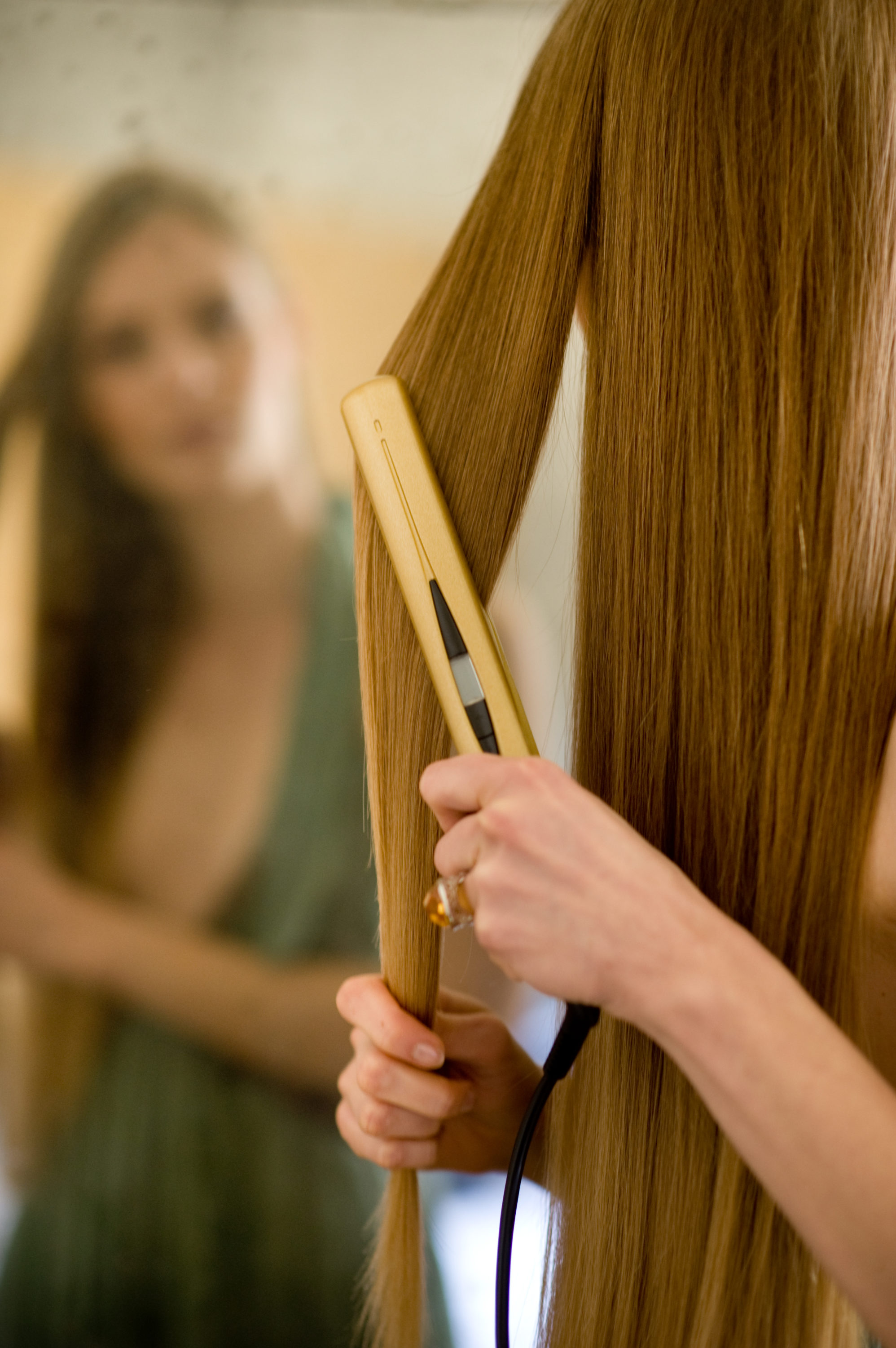 Foto di Donna di spalle si stira i capelli con la piastra allo specchio