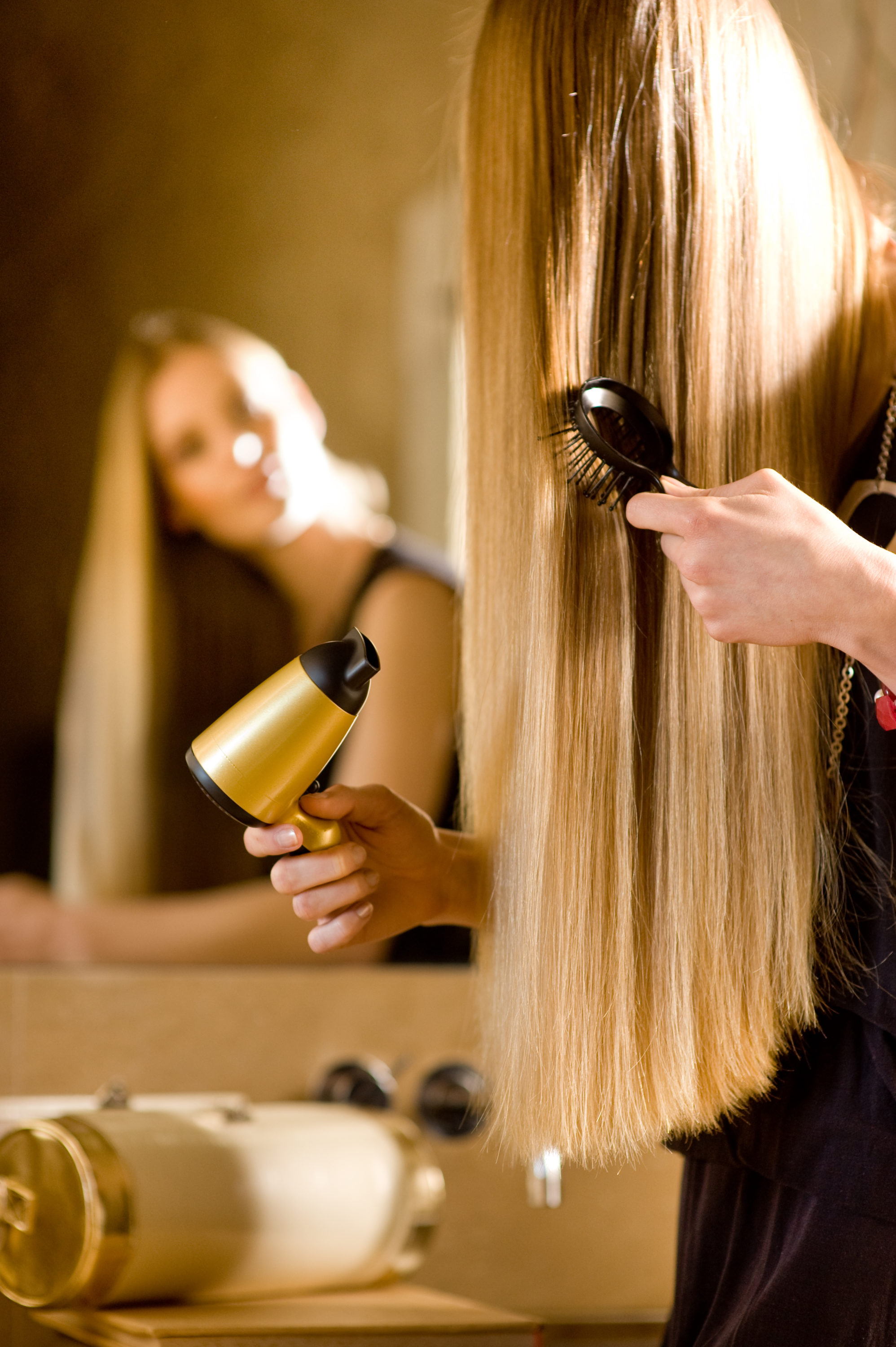 Foto di Donna di spalle si stira i capelli con la piastra allo specchio