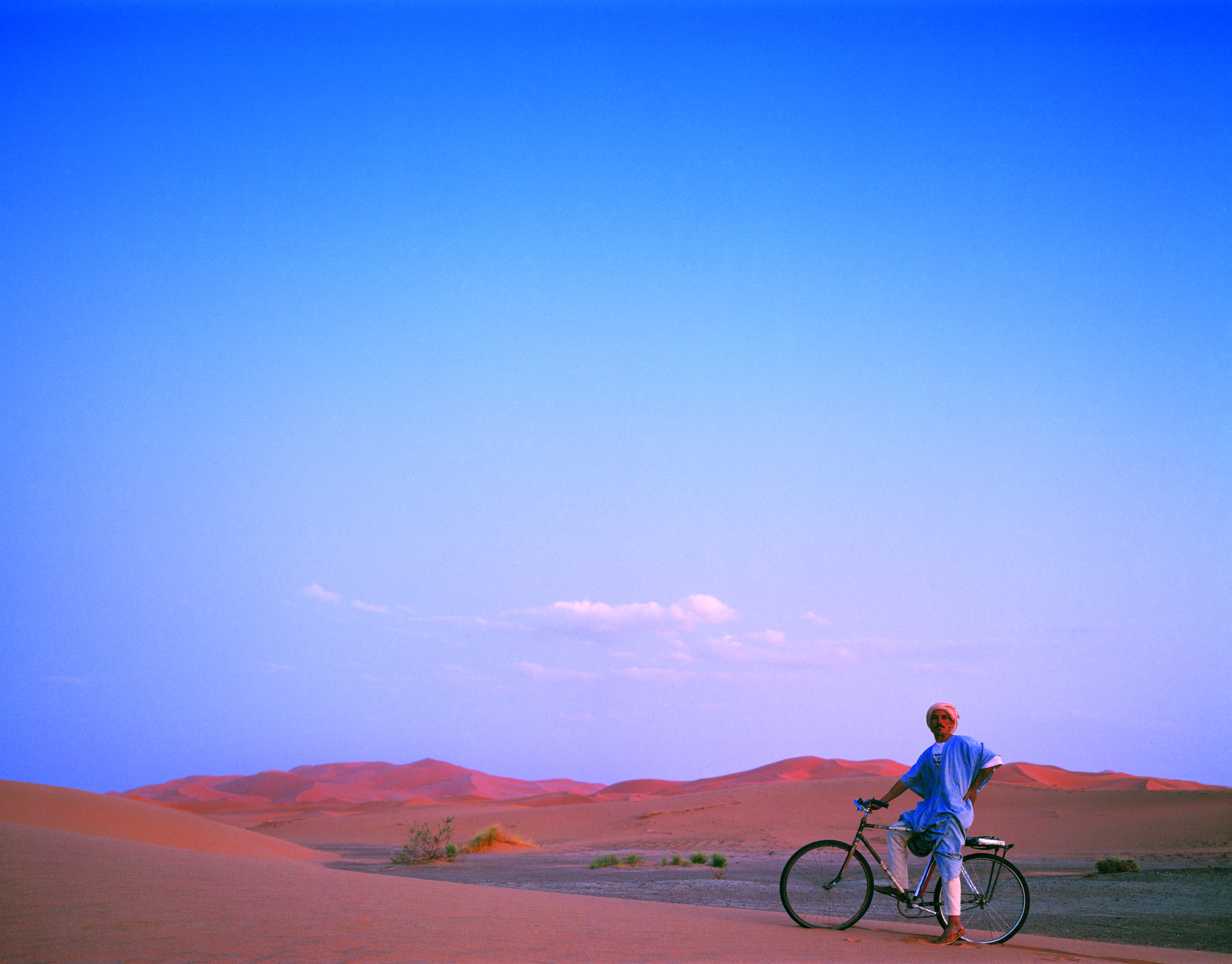 Uomo con bici nel deserto al tramonto