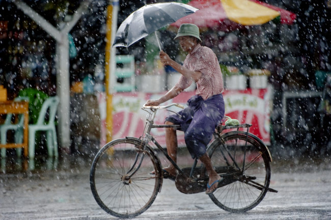 Uomo pedala sotto la pioggia in Myanmar