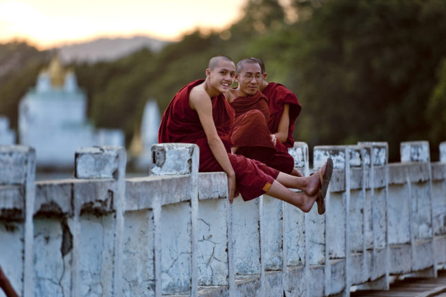 Monaci buddisti seduti su un ponte in Myanmar al tramonto