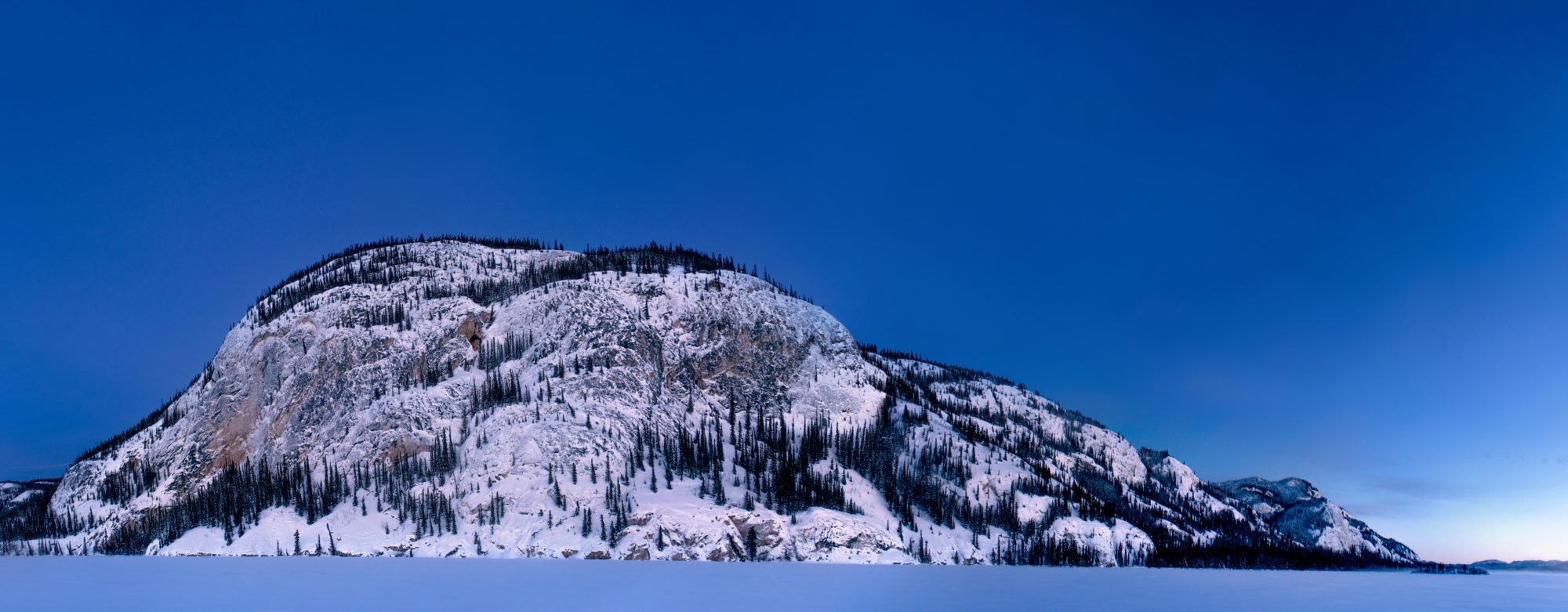 Foto di una montagna innevata emerge da un lago ghiacciato al crepuscolo