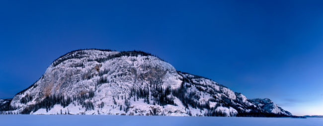 una montagna innevata emerge da un lago ghiacciato al crepuscolo