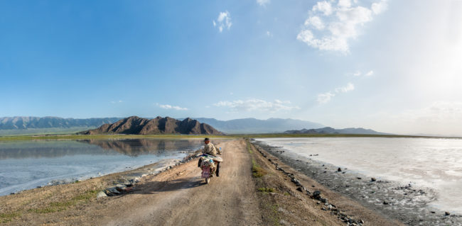 Lago Qinghai. Un uomo attraversa una diga in moto